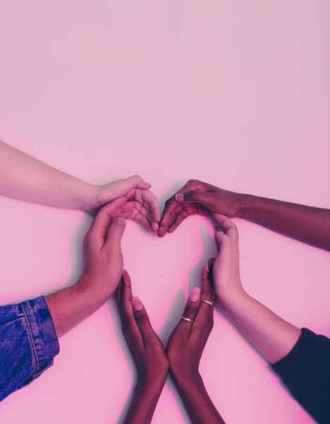 Image of six hands of various skin tones forming the shape of a heart with all of their fingers and hands together.